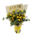 Mulher segurando bouquet de mini-rosas amarelas premium com eucalipto, embalado em papel bege com laço amarelo, coleção AMOR da Une Fleur dans la Ville.