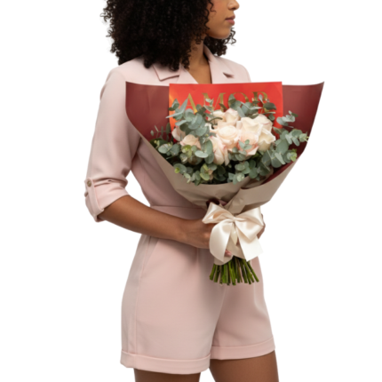 Mulher segurando um bouquet de rosas cor-de-rosa com folhagens elegantes, embalado em papel vermelho com laço cor-de-rosa, da Une Fleur dans la Ville.