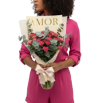 Mulher segurando um bouquet de rosas pink com folhagens elegantes, embalado em papel bege com laço creme, da Une Fleur dans la Ville.