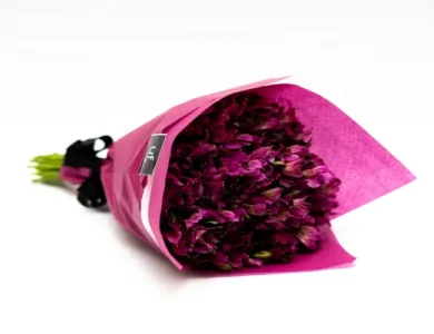 Bouquet de astromélias rosas, envolto com papel da mesma cor e laço preto.