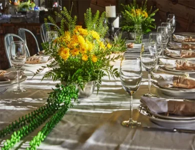 Mesa de jantar com arranjos florais amarelos com folhagem verde, um exemplo de decoração floral em jantares corporativos.