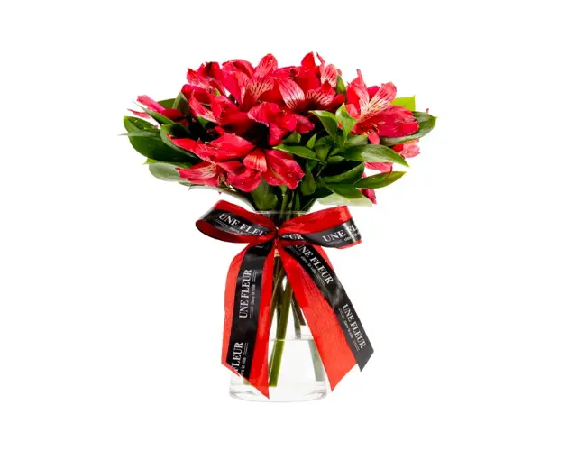Arranjo de rosas vermelhas e folhas verdes em vaso transparente com laço.