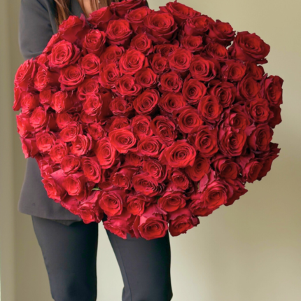 Mulher segurando um bouquet de 100 rosas vermelhas premium com laço preto personalizado, fundo neutro.