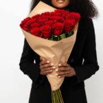 Mulher elegante segurando um buquê de 24 rosas vermelhas embaladas em papel kraft.
