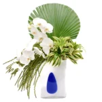 Arranjo contemporâneo com orquídeas brancas, folhagem exótica e vaso artesanal de vidro polonês com detalhe azul cobalto.