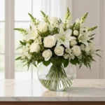 Arranjo de flores brancas com lírios e rosas em vaso redondo de vidro sobre mesa de mármore, representando a assinatura floral Magnifique da Une Fleur dans la Ville em São Paulo.