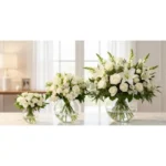 Três arranjos de flores brancas em vasos de vidro arredondados — versões Chic, Très Chic e Magnifique da assinatura floral Une Fleur dans la Ville — dispostos em ambiente elegante e iluminado.