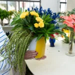 Arranjo tropical com rosas amarelas e flores azuis intensas em vaso vintage polonês de vidro amarelo da marca Alicja.