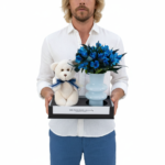 Kit presente com ursinho de pelúcia bege e arranjo de alstroemerias naturais pintadas de azul em vaso preto moderno, da Collection Monochrome Une Fleur dans la Ville, ideal para maternidade, nascimento e presentes românticos em São Paulo.