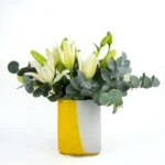 Arranjo de lírios brancos frescos com folhas de eucalipto em vaso de vidro polonês Alicja bicolor branco e amarelo – Une Fleur dans la Ville