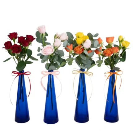 Quatro garrafinhas azuis com mini rosas vermelhas, rosadas, amarelas e laranja, com laços combinando, arranjadas lado a lado — Une Fleur dans la Ville.