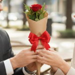 Mão masculina e feeminina segurando uma rosa colombiana vermelha embalada em papel craft