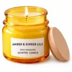 Vela aromática Amber and Ginger Lily acesa em frasco de vidro âmbar com tampa de madeira ao lado