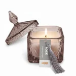 Vela Perfumada Rock acesa em pote de vidro cinza decorativo com tampa e tassel