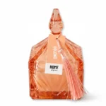 Vela aromática em pote de vidro facetado âmbar/rose gold com tampa pontiaguda trabalhada e pingente de tassel em tom pêssego, fragrância Uolong Home Fragrance.